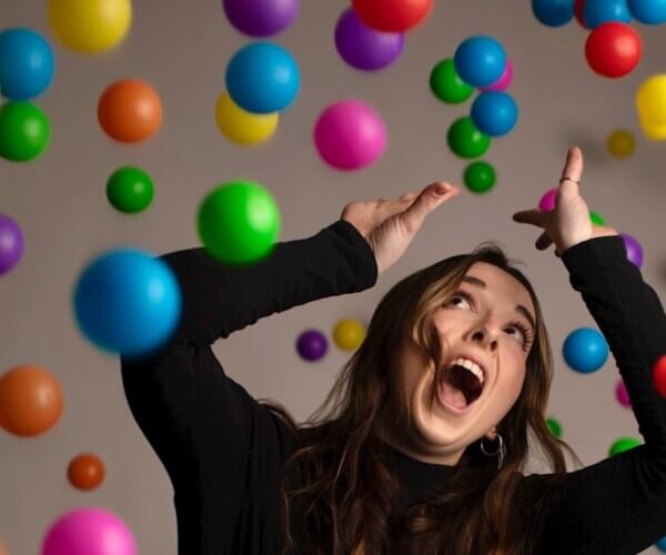 a woman in a black shirt and jeans is surrounded by balloons